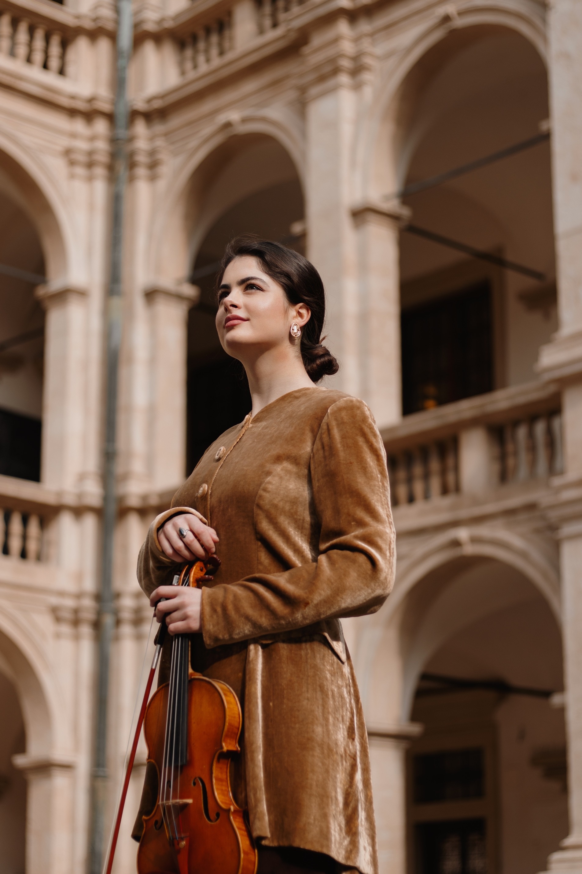 Marley Erickson standing in a stone courtyard holding a violin.